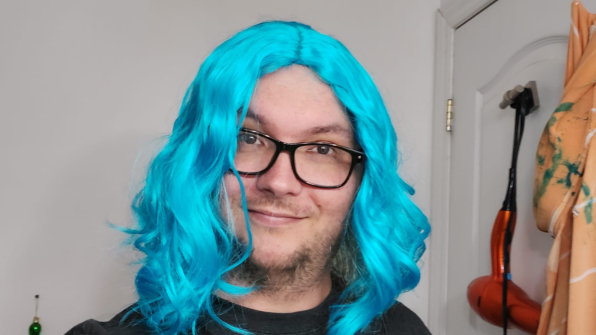 A man wearing a black shirt wears a long bright blue wavy costume wig